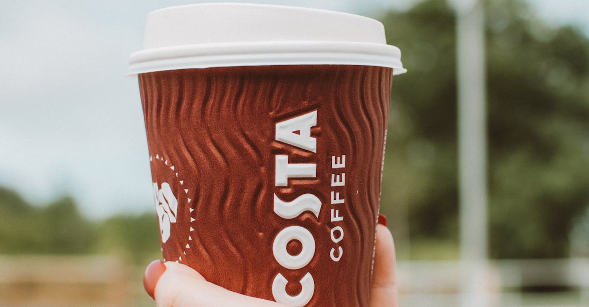 Close-up of a hand holding a Costa Coffee cup in an outdoor setting on a clear day.