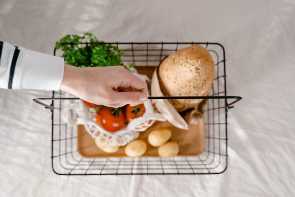 A hand holding a wire shopping basket filled with fresh groceries